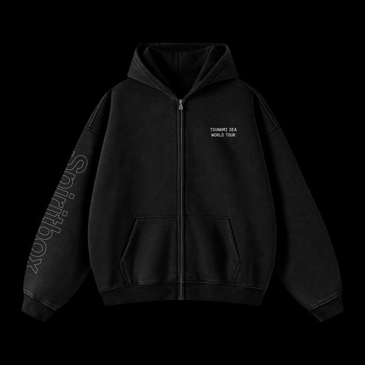 A black zip-up hoodie from Spiritbox featuring TURNMT SEA WORLD TOUR text on the left chest and Shiftbox printed down the right sleeve, displayed on a plain black background—ideal for fans of bold printed apparel.