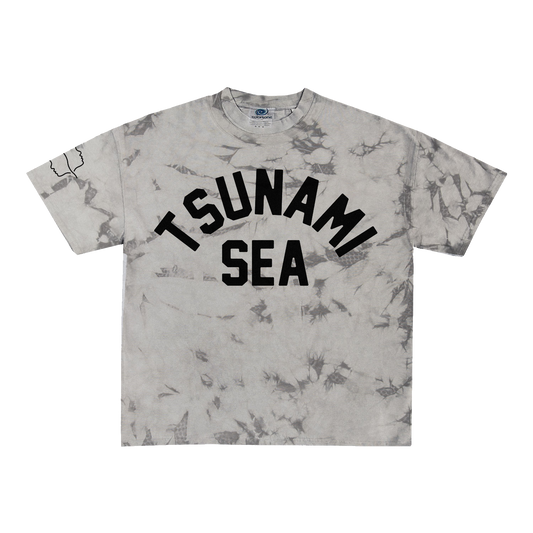 A Spiritbox gray crystal dye t-shirt featuring bold black "TSUNAMI SEA" text across the chest and a small black outlined graphic on the left sleeve.